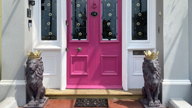 A pink door with a number plate, flanked by two lion statues wearing crowns, and a white door with a window above. - Aberley House (Liverpool)