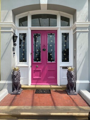 A pink door with a number plate, flanked by two lion statues wearing crowns, and a white door with a window above. - Aberley House (Liverpool)