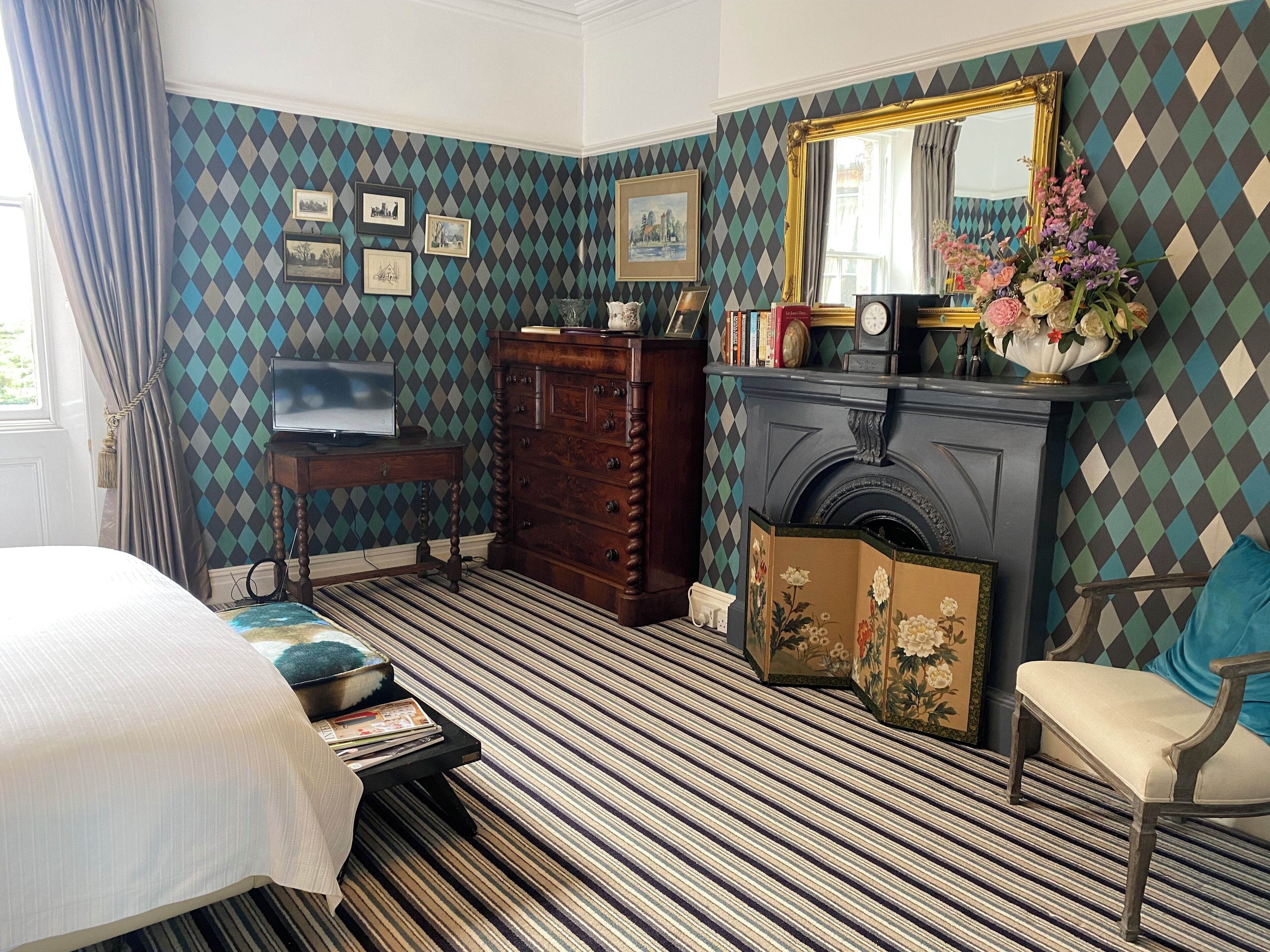Una habitación con papel tapiz estampado, una chimenea, un espejo y una cama.