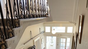 A grand staircase with ornate black railings and beige carpeted steps leading to a bright room with a large window and a view of the outdoors. - Aberley House (Liverpool)