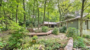 Une cabane entourée d’une forêt dense, dotée d’une terrasse en bois et d’un petit étang.