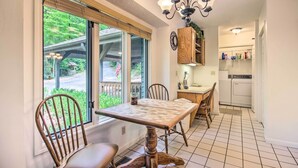 Un espace repas avec une table et des chaises en bois, un lustre et une vue dégagée grâce à de grandes fenêtres.