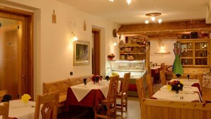 Un'accogliente sala da pranzo con tavoli e sedie in legno, una vetrina con dolci e un'atmosfera calda e invitante.