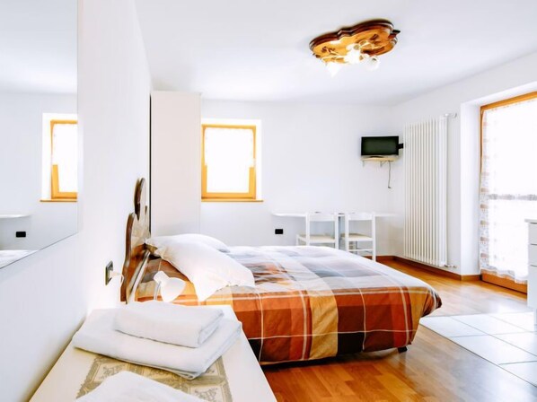A modern bedroom with a large bed, a desk, and a TV.
