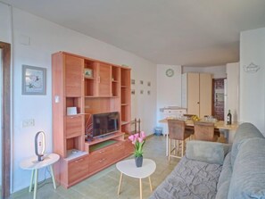 Un salon comprenant un canapé, un téléviseur, des étagères en bois et un coin repas avec une table et des chaises.