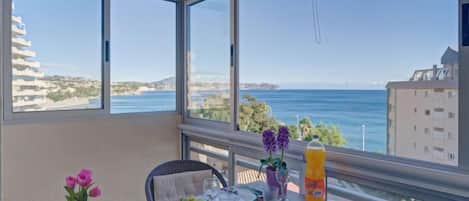 A balcony with a table set for a meal, overlooking a coastal view.