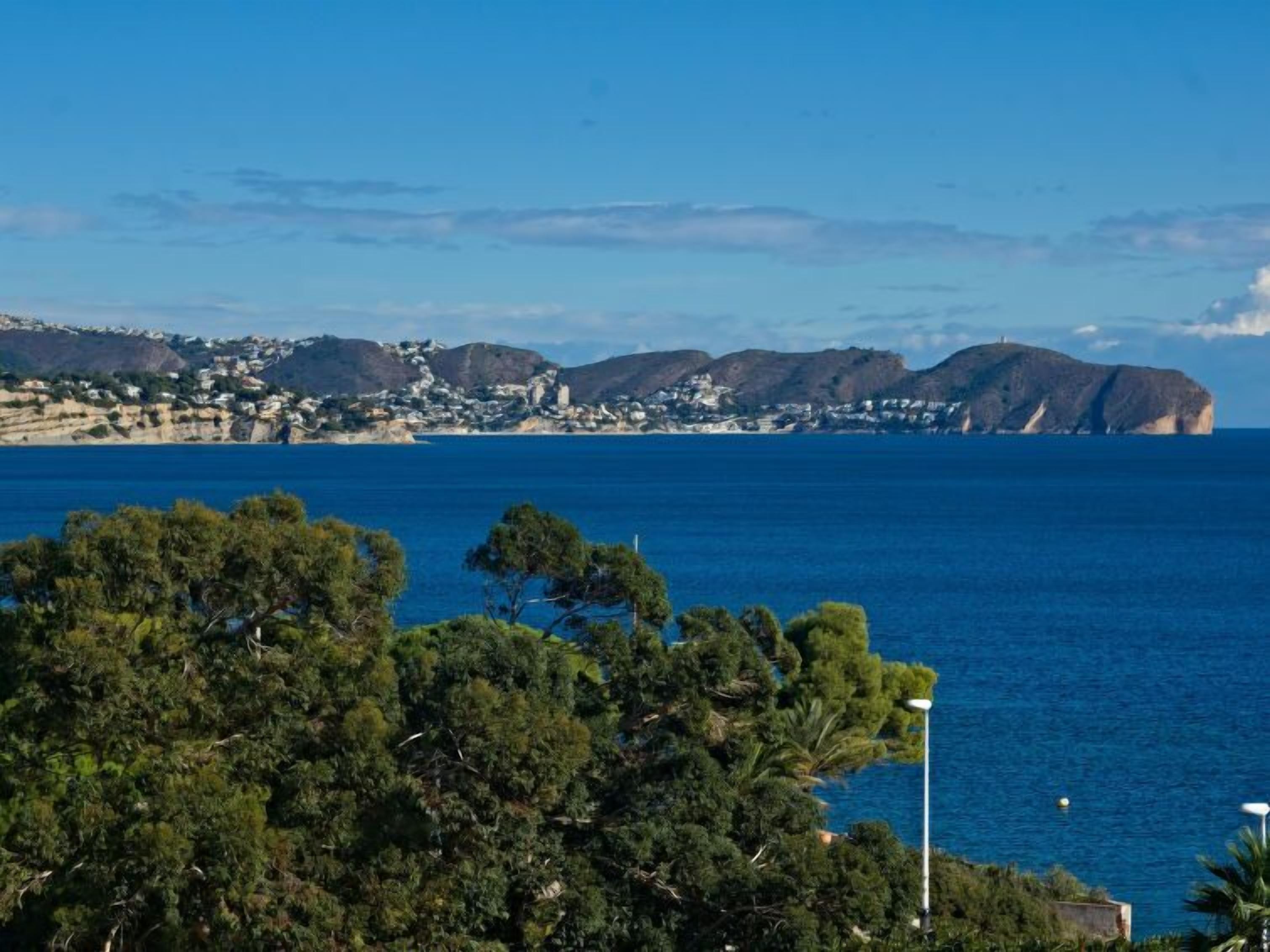 A coastal landscape with a view of the sea, a town in the background, and a prominent hill.