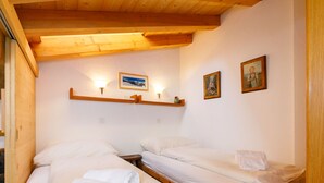 Ein kleines, gemütliches Zimmer mit zwei Holzbettställen, weißen Leinen und einer Holzbalkendecke.