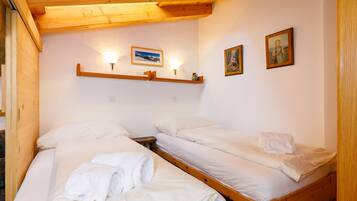 Une petite pièce agréable et chaleureuse, avec deux lits superposés en bois, du linge de lit blanc et un plafond en bois.
