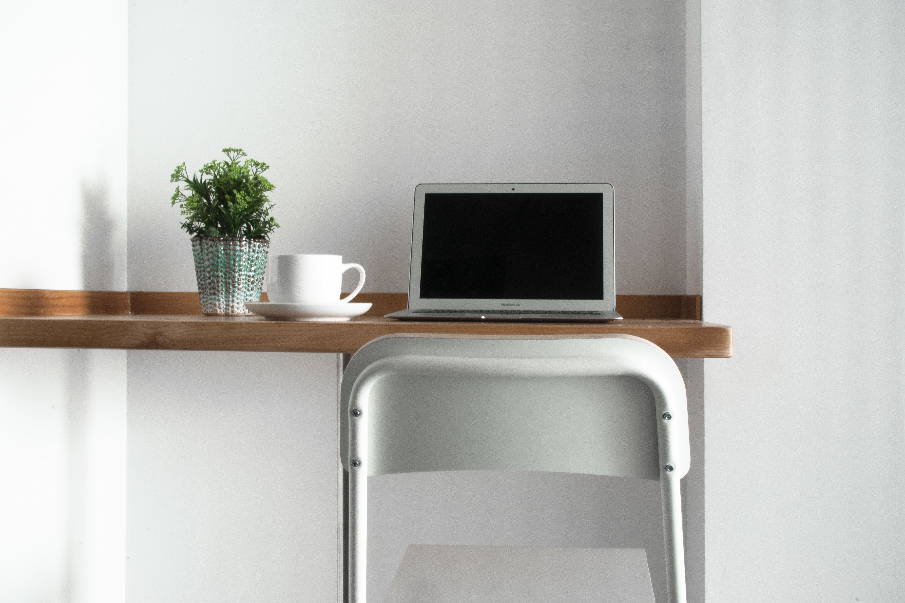 A laptop on a wooden shelf, a white chair, and a potted plant.