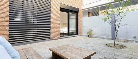 Une terrasse extérieure moderne avec une table en bois, un mur en briques et un petit arbre.