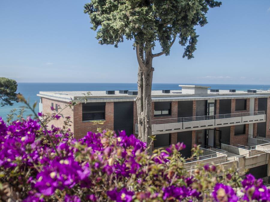 A modern building with a flat roof and large windows, overlooking a body of water.