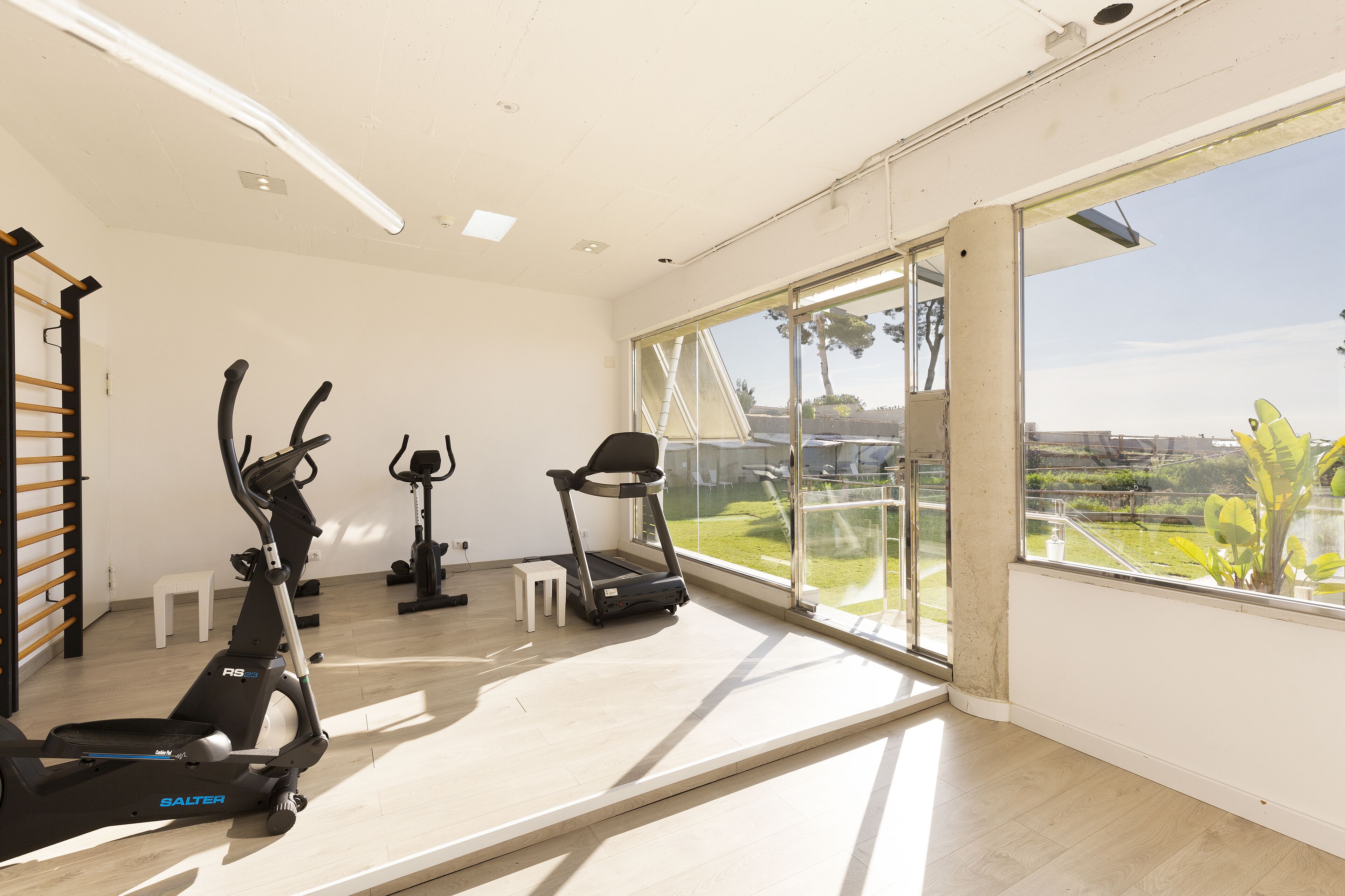 A spacious room with a large window, a treadmill, an elliptical, and a stationary bike.