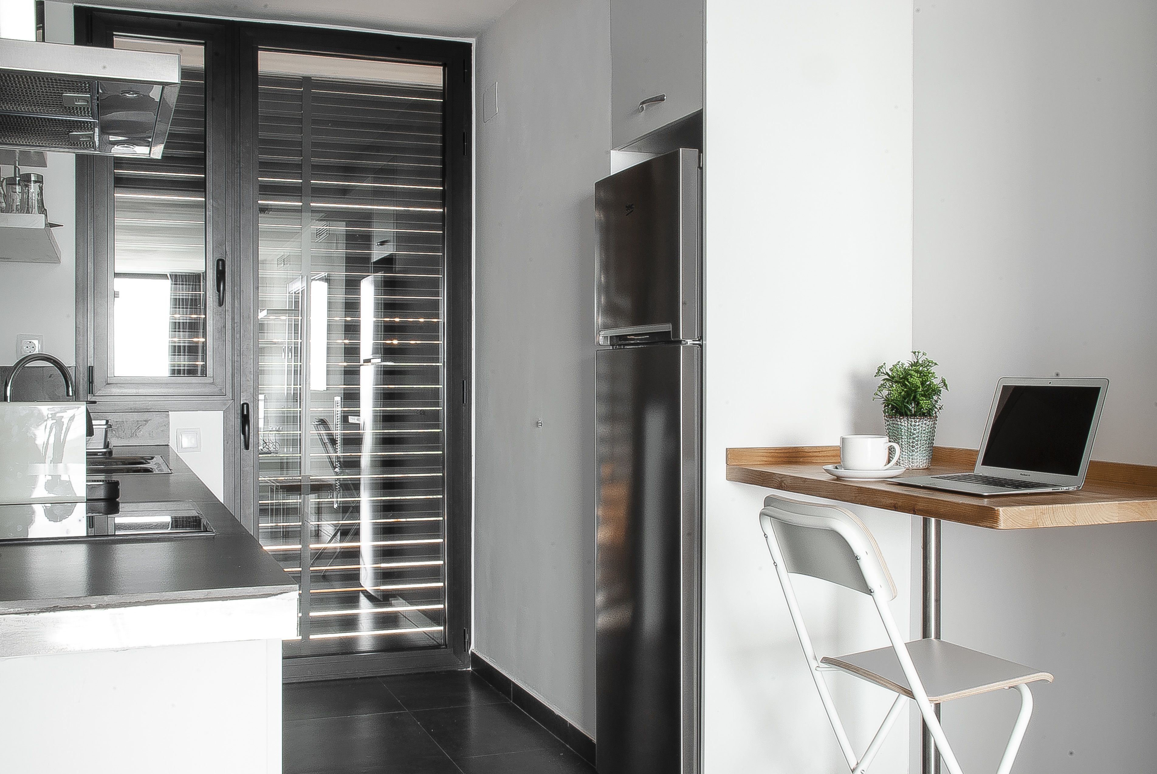 A modern kitchen with a stainless steel refrigerator, a built-in oven, and a window with blinds.