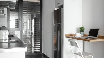 A modern kitchen with a stainless steel refrigerator, a built-in oven, and a window with blinds.