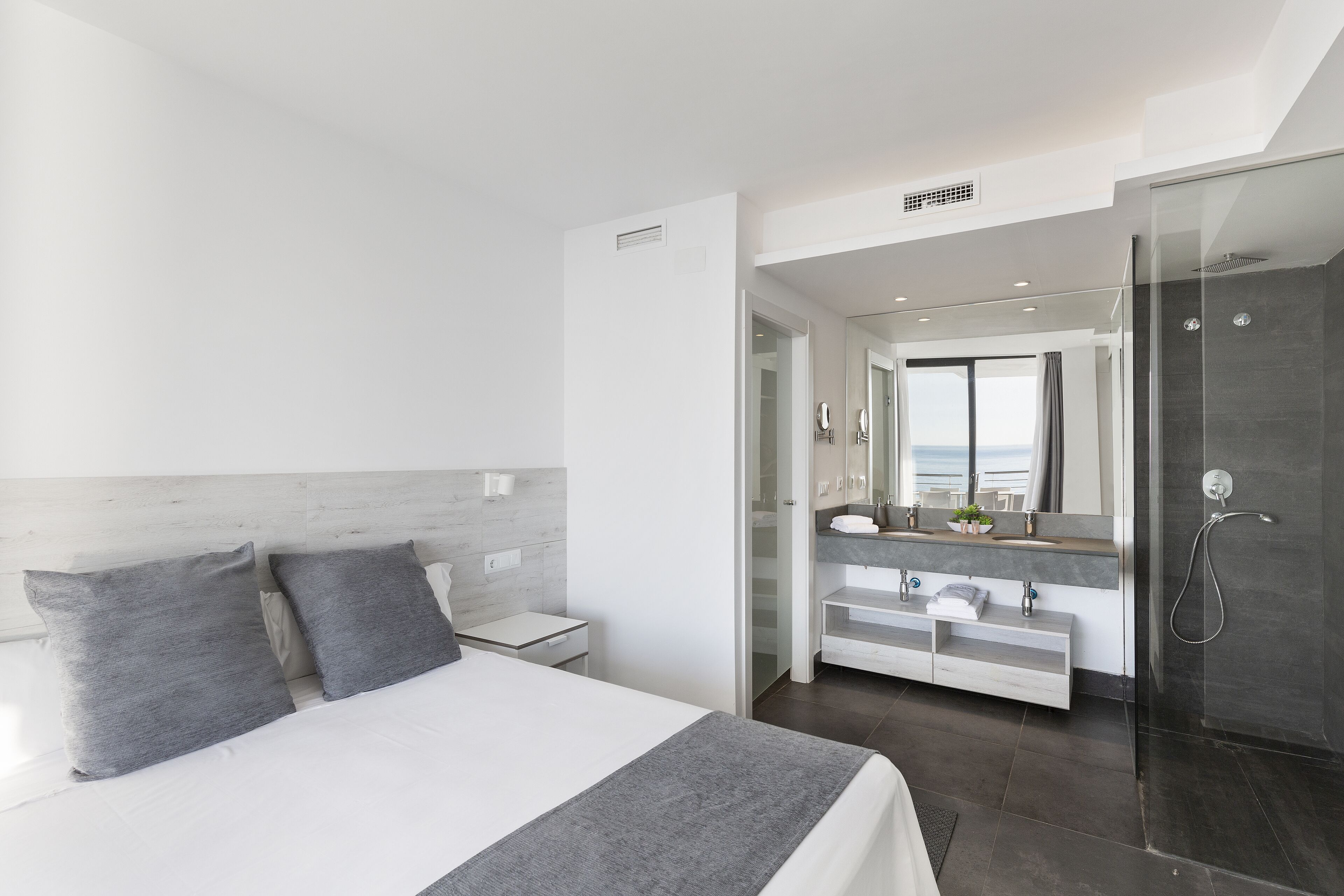 A modern hotel room with a large bed, a walk-in closet, a bathroom with a glass shower, and a view of the city.