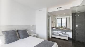 A modern hotel room with a large bed, a walk-in closet, a bathroom with a glass shower, and a view of the city.