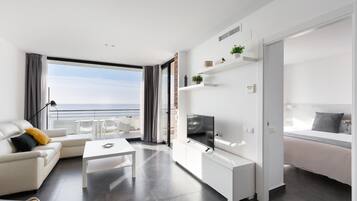 A modern living room with a sofa, coffee table, TV, and a balcony with a view of the sea.