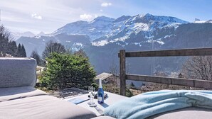 A mountain view from a balcony with a wooden railing, a sofa, and a table with glasses and a bottle. - Roossi Apt. 1 by Interhome (Wengen)