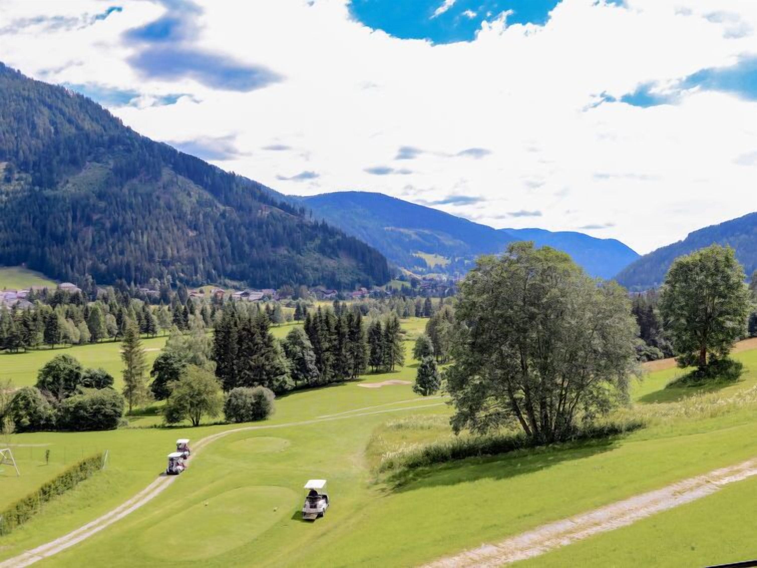 A golf course with a clear path, surrounded by lush greenery and mountains in the background.