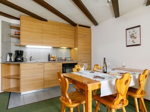 A modern kitchen with wooden cabinets, a dining table set with chairs, and a small dining area. - Residenza Chesa Margun 45-1 by Interhome (Silvaplana-Surlej)