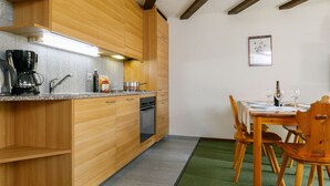 A compact kitchen with wooden cabinets, a built-in dishwasher, and a dining area with a table and chairs. - Residenza Chesa Margun 45-1 by Interhome (Silvaplana-Surlej)