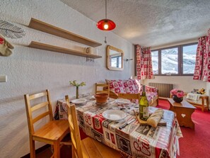 A cozy room with a dining table set for two, a bed with patterned bedding, a mirror, and a window with curtains. - Arcelle 604 by Interhome (Val Thorens)