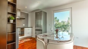 A modern kitchen with a glass dining table, white chairs, and a view of the outdoors. - Apartment Karmen by Interhome (Umag)