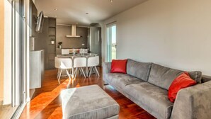 A modern living room with a grey sofa, a glass dining table, and a grey ottoman. - Apartment Karmen by Interhome (Umag)