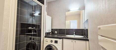 Uma casa de banho compacta com chuveiro, máquina de lavar e lavatório.