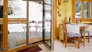 A cozy room with a wooden dining table, chairs, and a sliding glass door leading to a snowy outdoor area. - Residenza Chesa Margun 34-6 by Interhome (Silvaplana-Surlej)