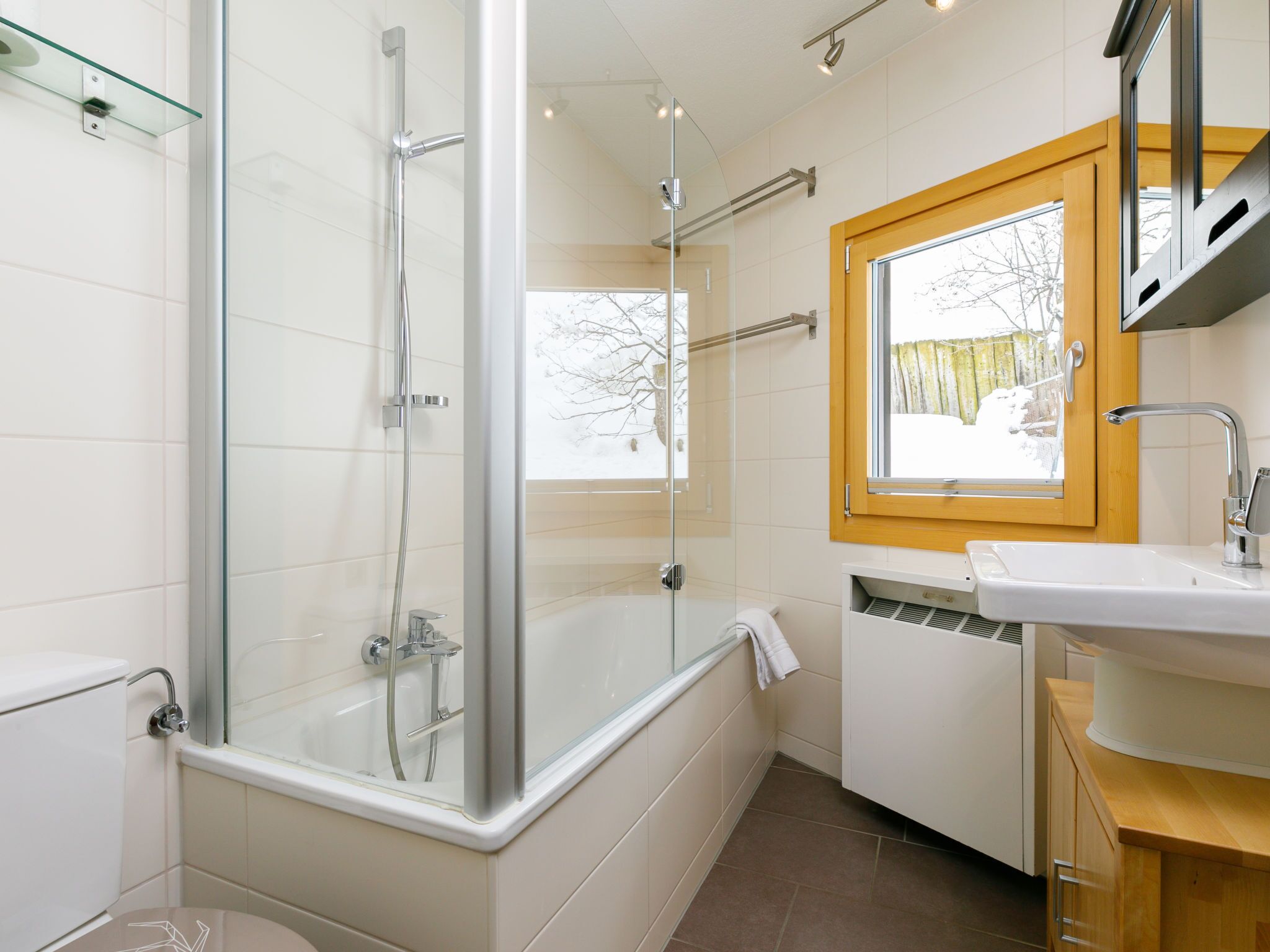 Un baño moderno con ducha de vidrio, un lavamanos blanco y una ventana con vistas a árboles.