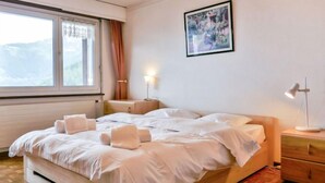 Une chambre à coucher avec un lit, des lampes de chevet, une table de nuit, une fenêtre avec des rideaux et un tableau au mur.