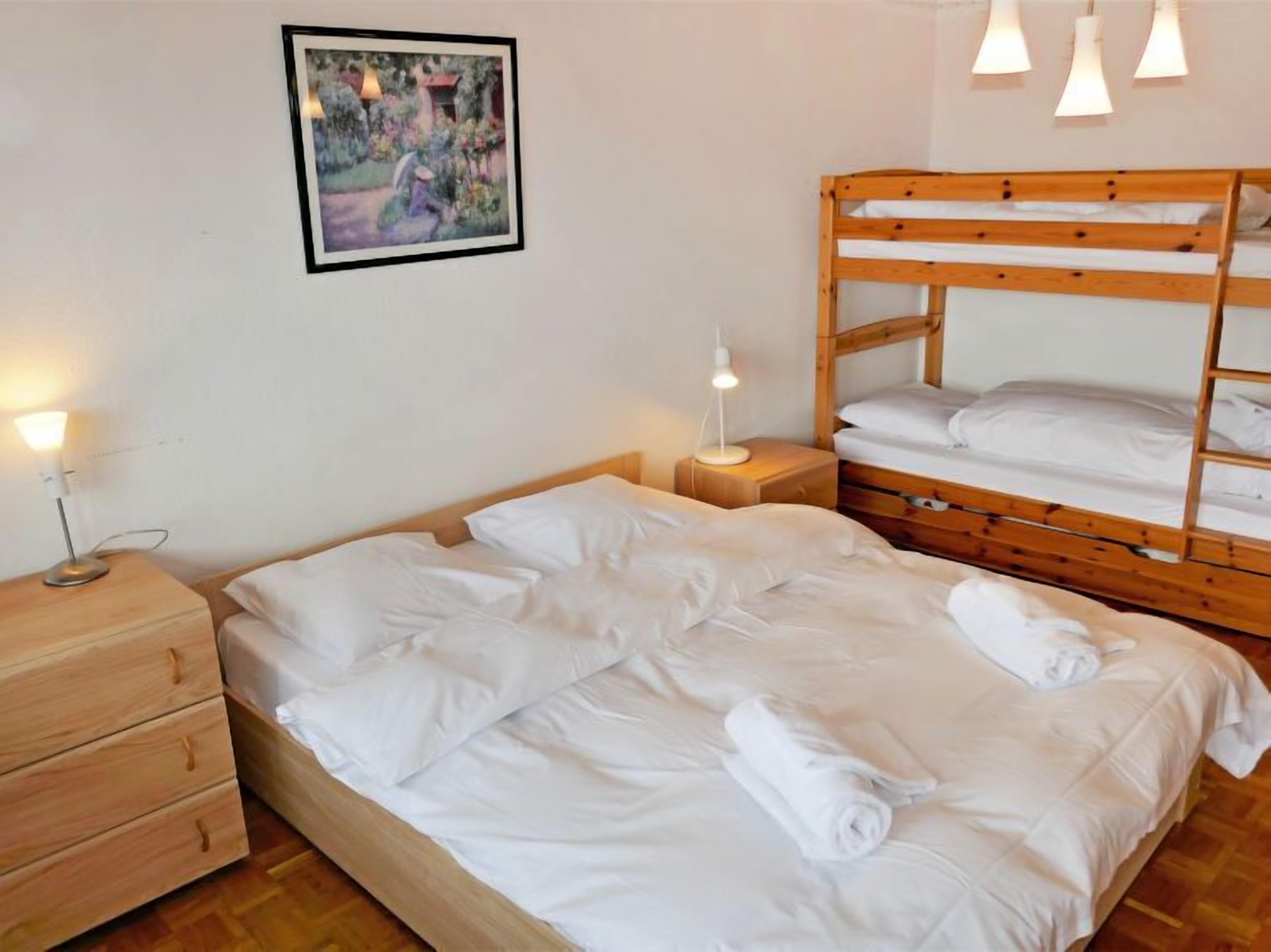 Ein Schlafzimmer mit Etagenbett, Nachttisch mit Lampe, Holzkommode und einem gerahmten Bild an der Wand.