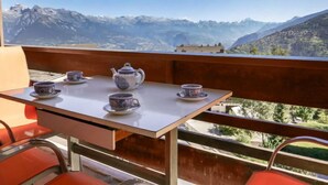 Un balcon avec une table dressée pour le thé, offrant une vue sur un paysage montagneux.