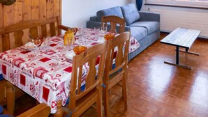 Un coin repas avec une table dressée pour quatre personnes, des chaises en bois, une nappe à motifs et un canapé en arrière-plan.
