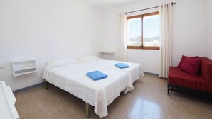Una habitación sencilla con dos camas, una ventana con cortinas, un sofá rojo y un estante blanco.