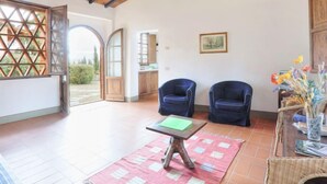 A spacious room with a high wooden ceiling, two blue armchairs, a small table with a green folder, and a wicker side table with a vase of flowers. - Il Mandorlato by Interhome (Impruneta)