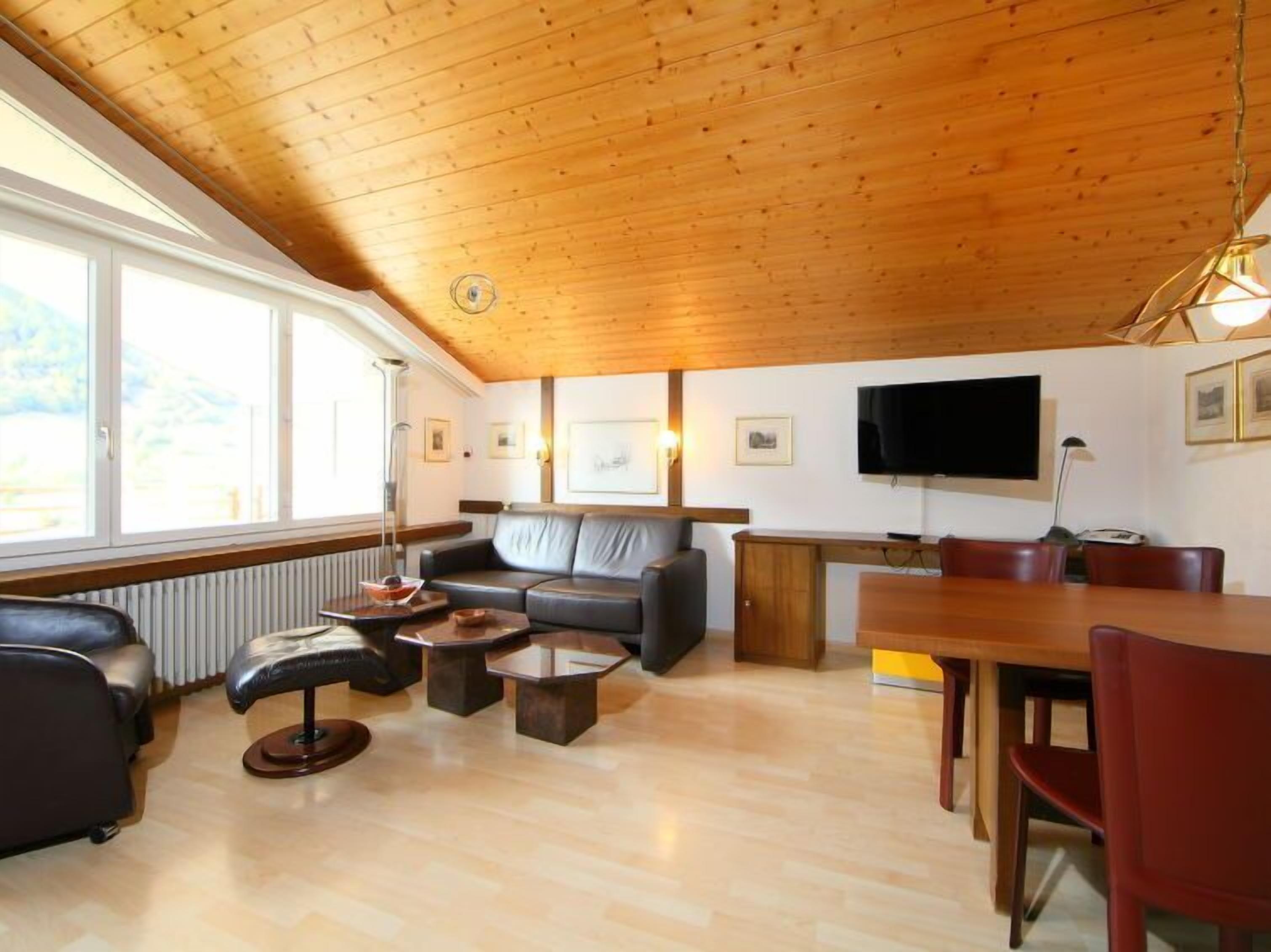 Un soggiorno accogliente con soffitto in legno, un divano, un tavolino da caffè, una TV e una zona pranzo con sedie.