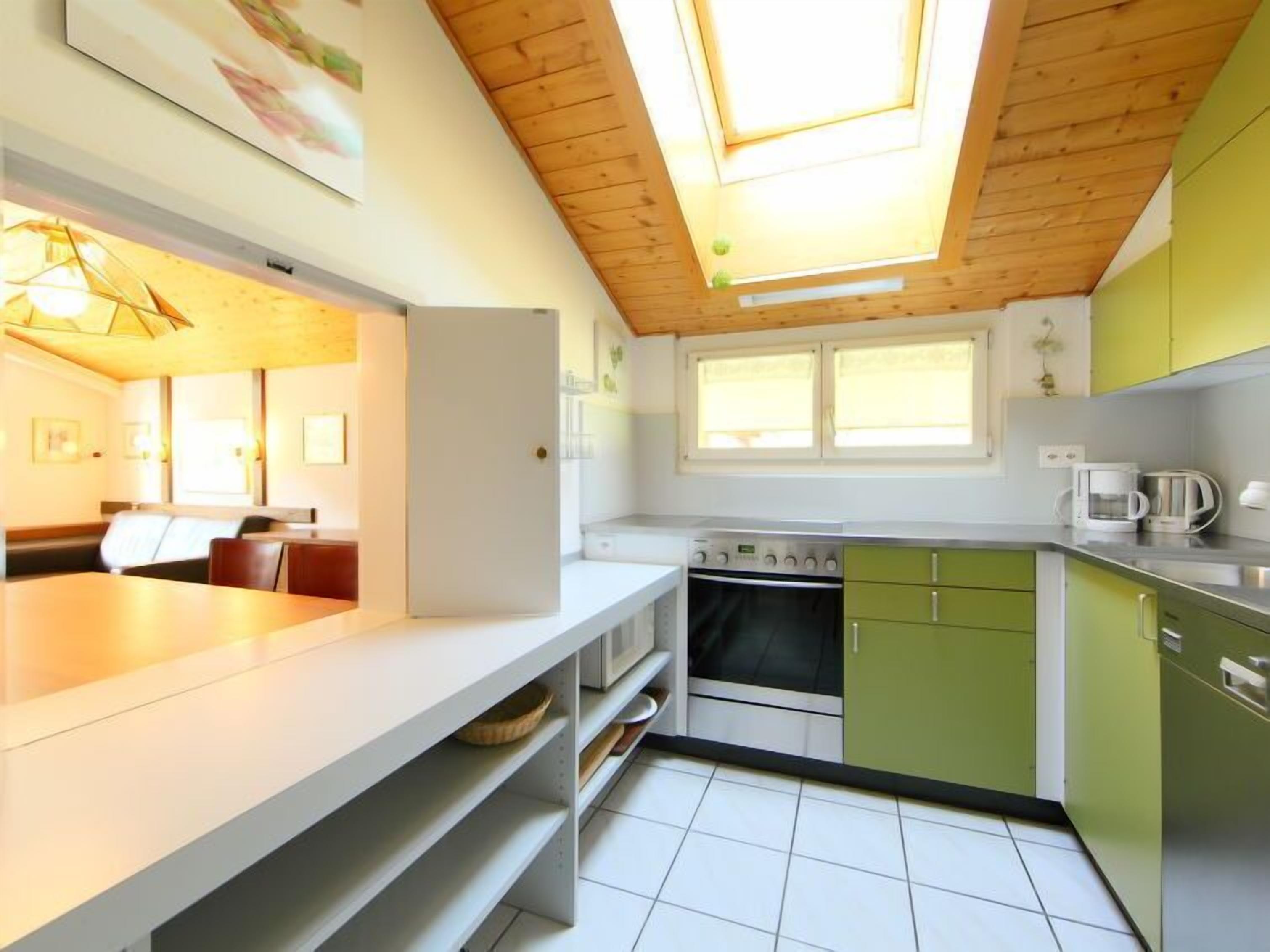 A modern kitchen with a skylight, green cabinets, and a dining area with a table and chairs.