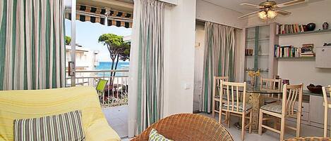 A room with a balcony, wicker furniture, a dining table with chairs, and a ceiling fan.