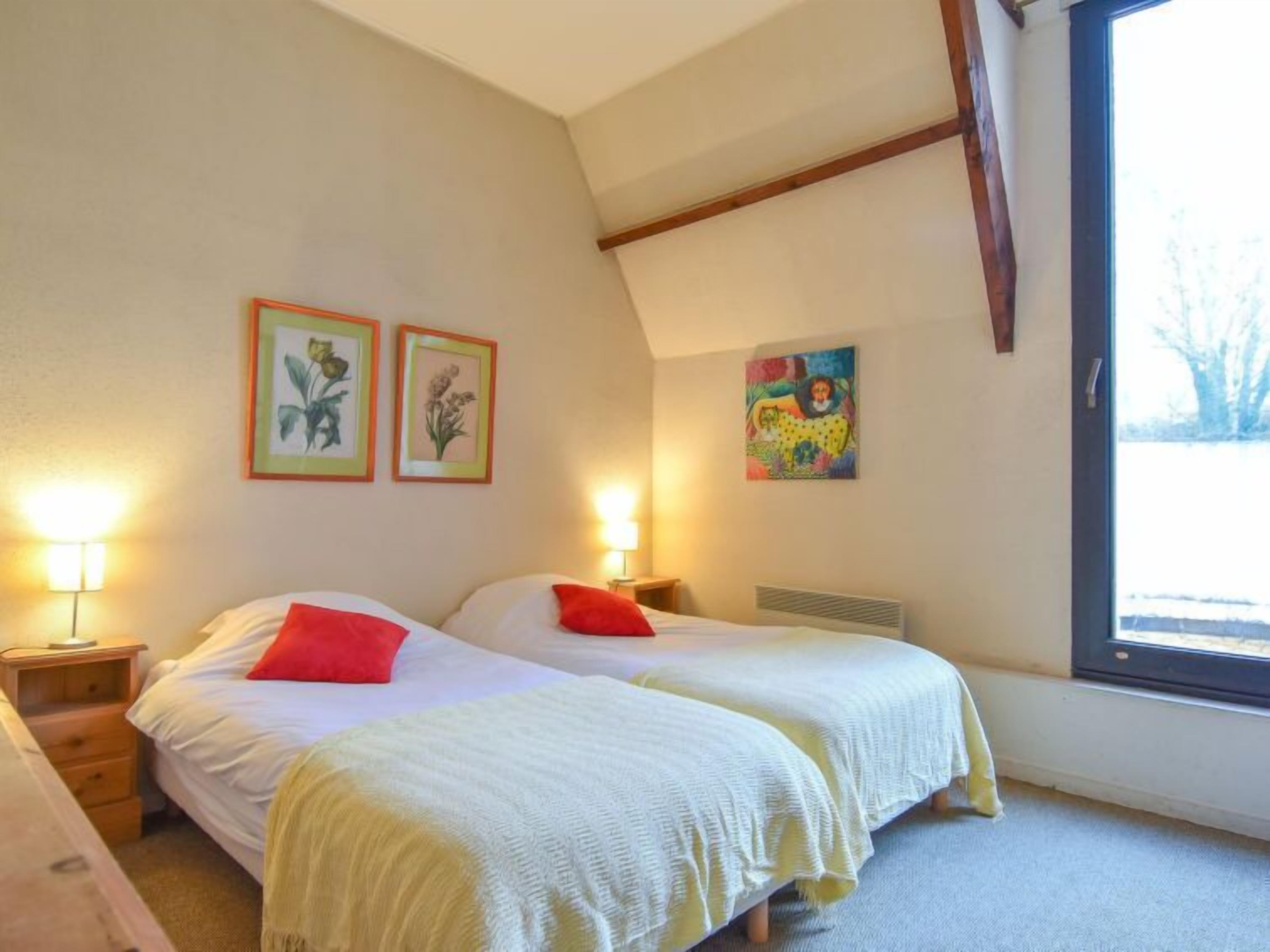 A bedroom with two beds, each with a red pillow, and framed botanical prints on the wall.