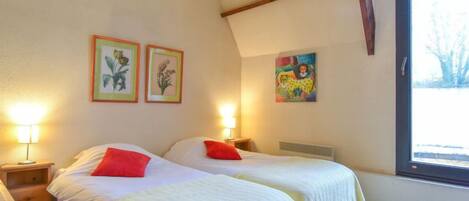 A bedroom with two beds, each with a red pillow, and framed botanical prints on the wall.