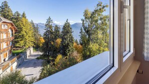 Vista de la montaña desde una ventana con vistas a un bosque y un edificio con balcón.