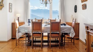 Comedor con una mesa dispuesta para cuatro, sillas de madera, una araña y vistas a montañas a través de amplios ventanales.