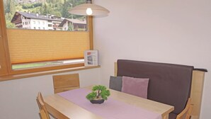 Ein kleiner Essbereich mit Tisch, Stühlen, einer Bank, einem Blumentopf und einem Fenster mit Blick auf Häuser.
