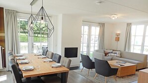 A modern living room with a dining area, large windows, and a flat-screen TV. - Vacation home Alk 8 by Interhome (Noordwijk)