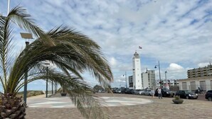 A paved plaza with palm trees, a tall white tower, and parked cars. - Vacation home Alk 8 by Interhome (Noordwijk)