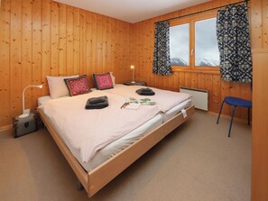 A wooden-paneled bedroom with a bed, pillows, a nightstand, a window with curtains, and a chair.