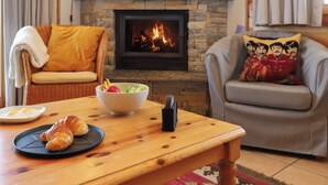A cozy living room with a fireplace, a dining table with croissants, and a bowl of fruit. - Vacation home Lara by Interhome (Nendaz)